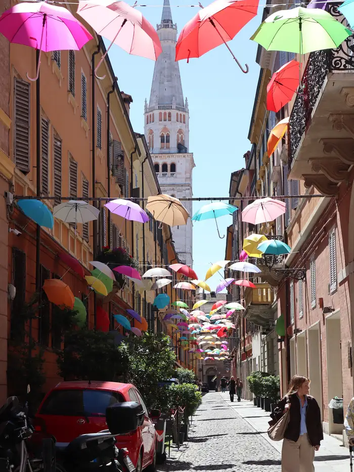 Coloured umbrellas strung above a street below the Ghirlandina tower, Modena, Italy